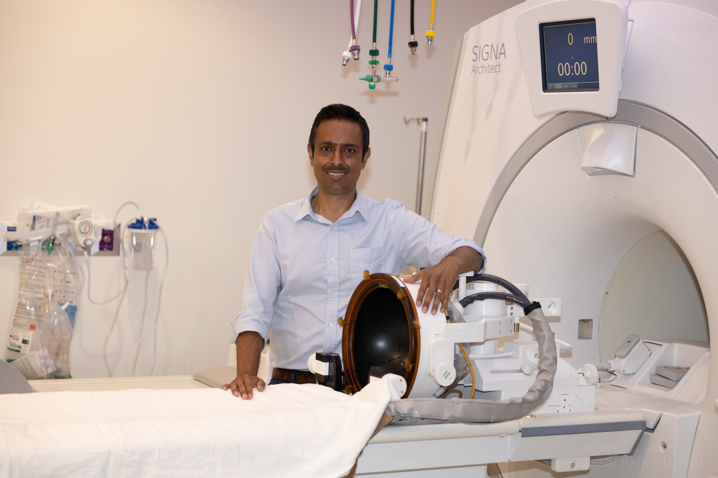 Dr. Bari standing beside the focused ultrasound transducer helmet on the table of the 3T MRI scanner in the treatment suite